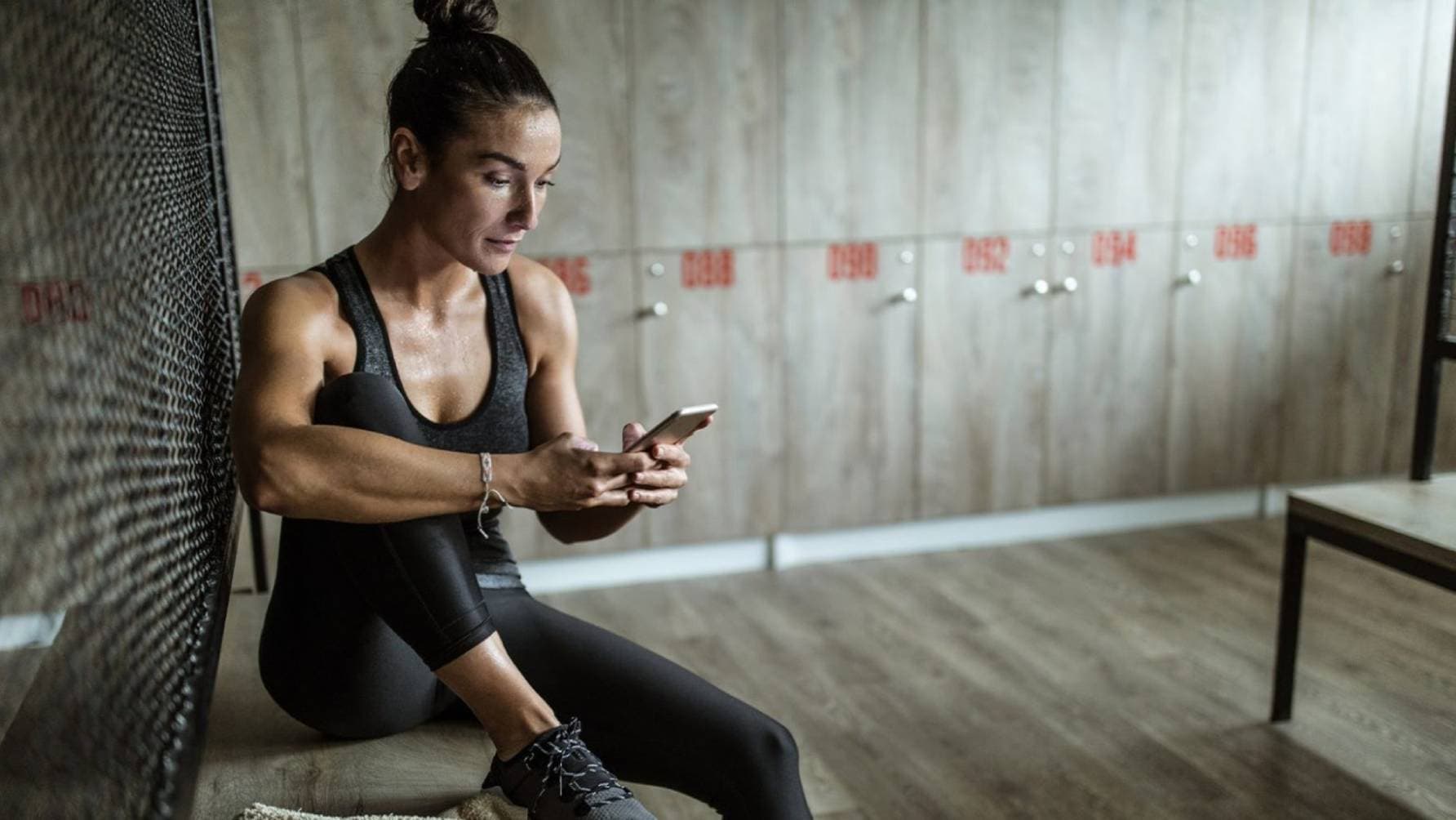 A woman in athletic wear seated while engrossing in her phone