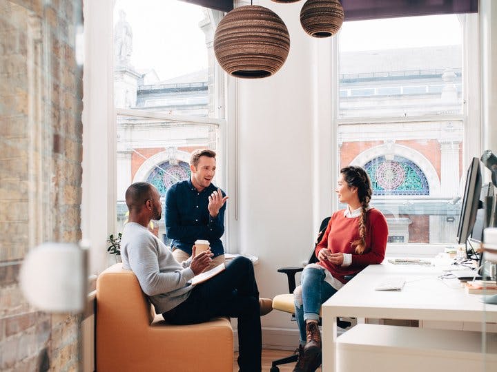 Three workers at a startup engaged in discussion in their office
