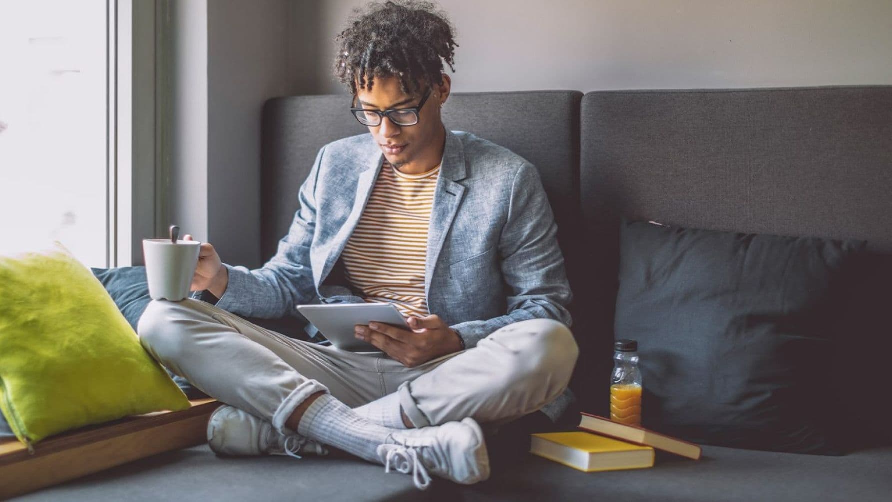 A man seated with a cup while watching on a tablet.
