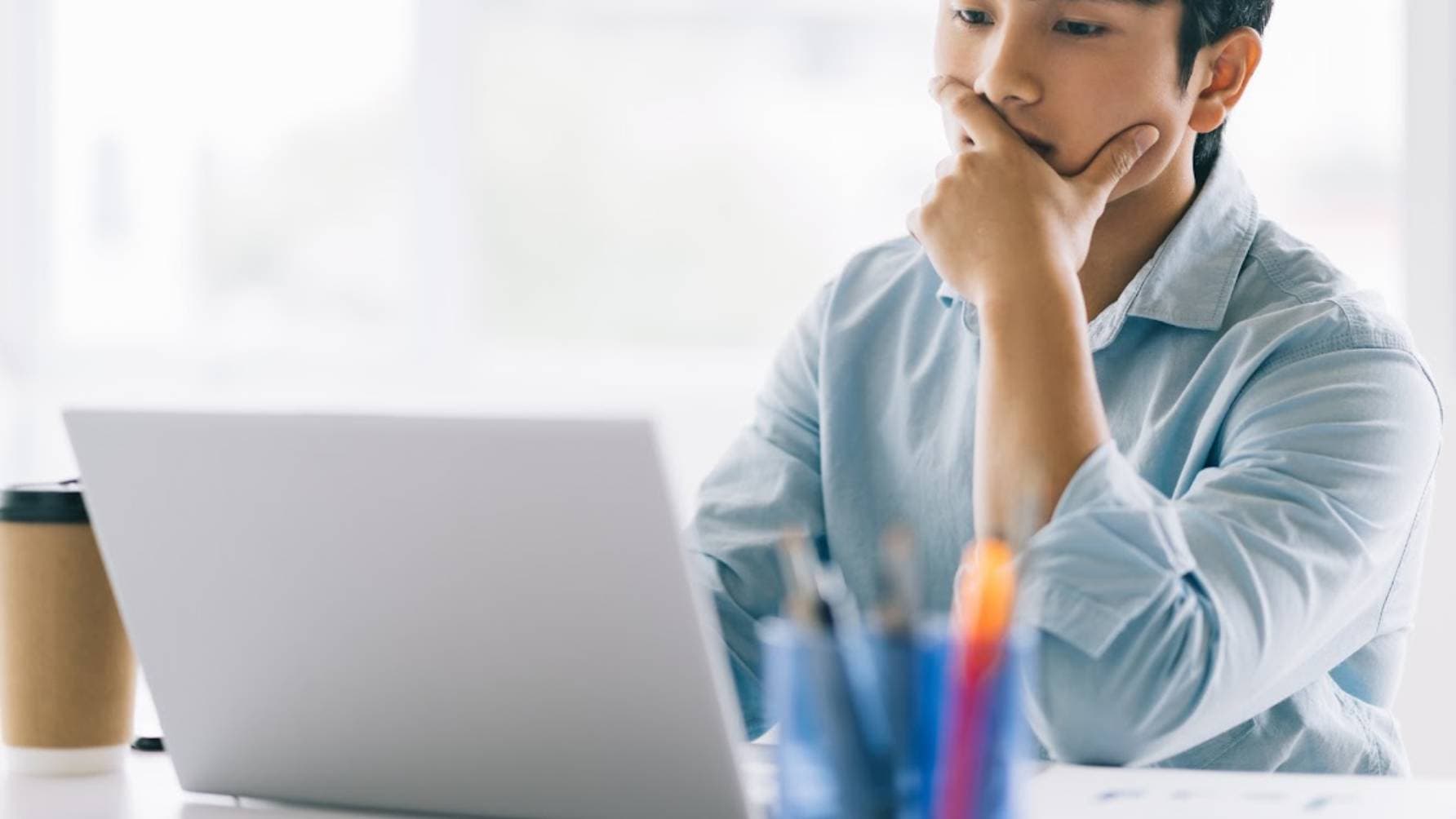 person sitting with a furrowed brow, anxiously holding his mouth as he awaits the completion of a processing task on his laptop