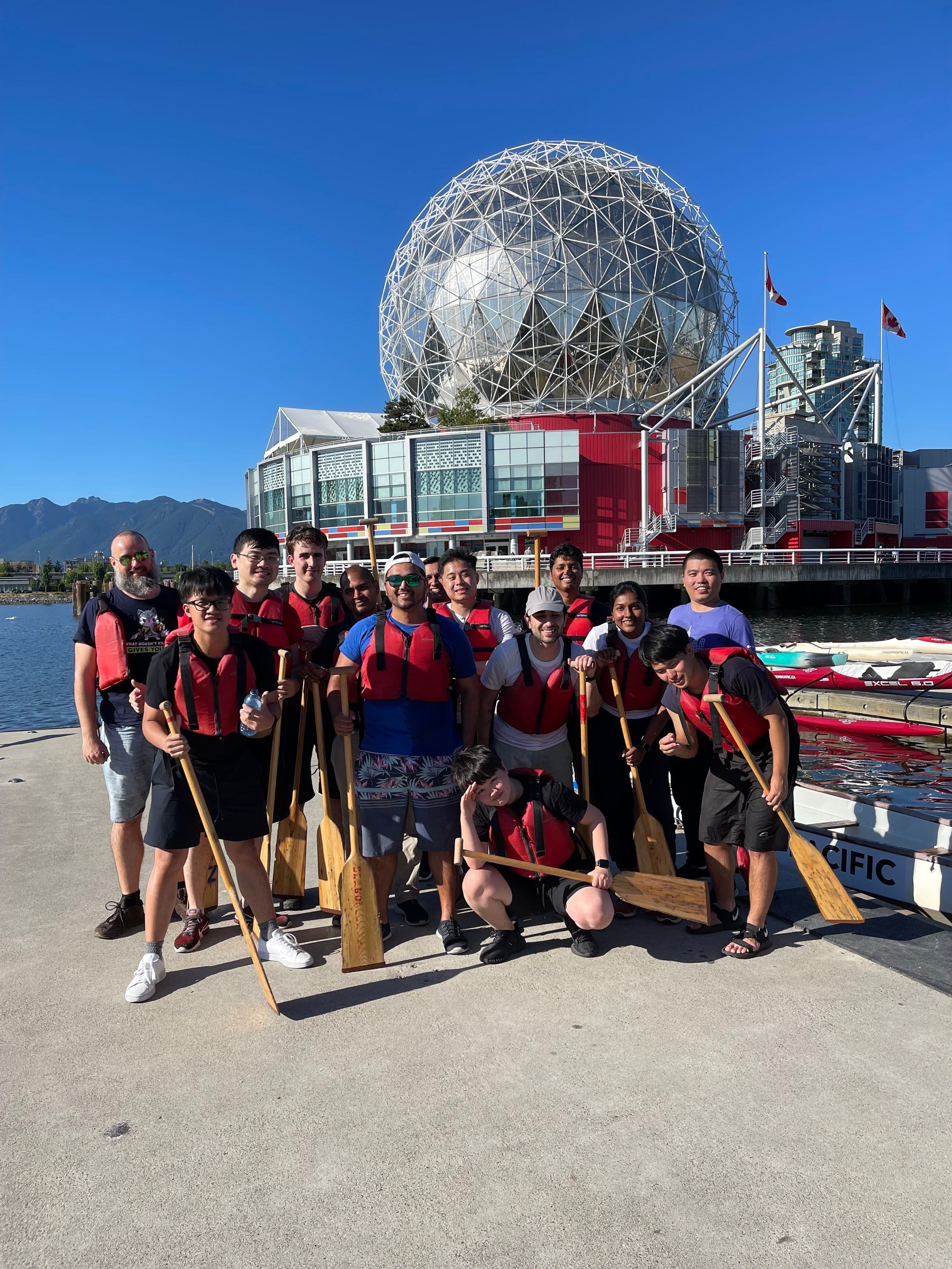 A group of coworkers posing with paddles in front of their boat.