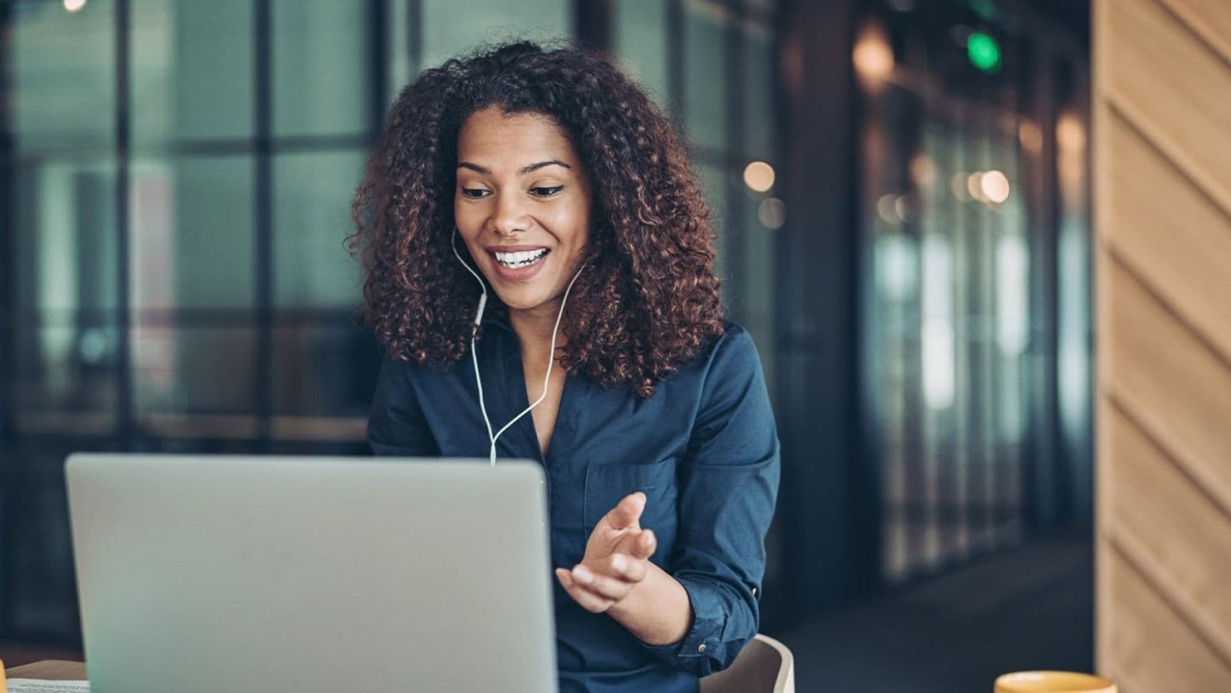 A woman beaming with joy while wearing earphones and talking on her laptop.