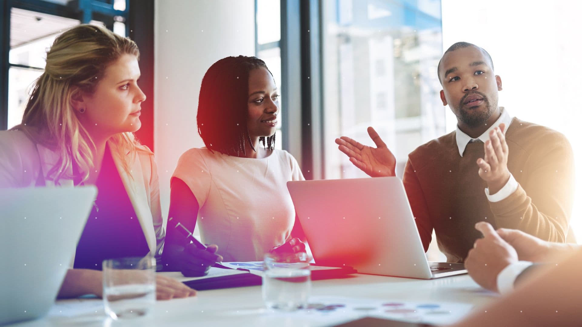 Team meeting in a modern office with professionals collaborating around laptops and documents, featuring a colorful tech-inspired overlay.
