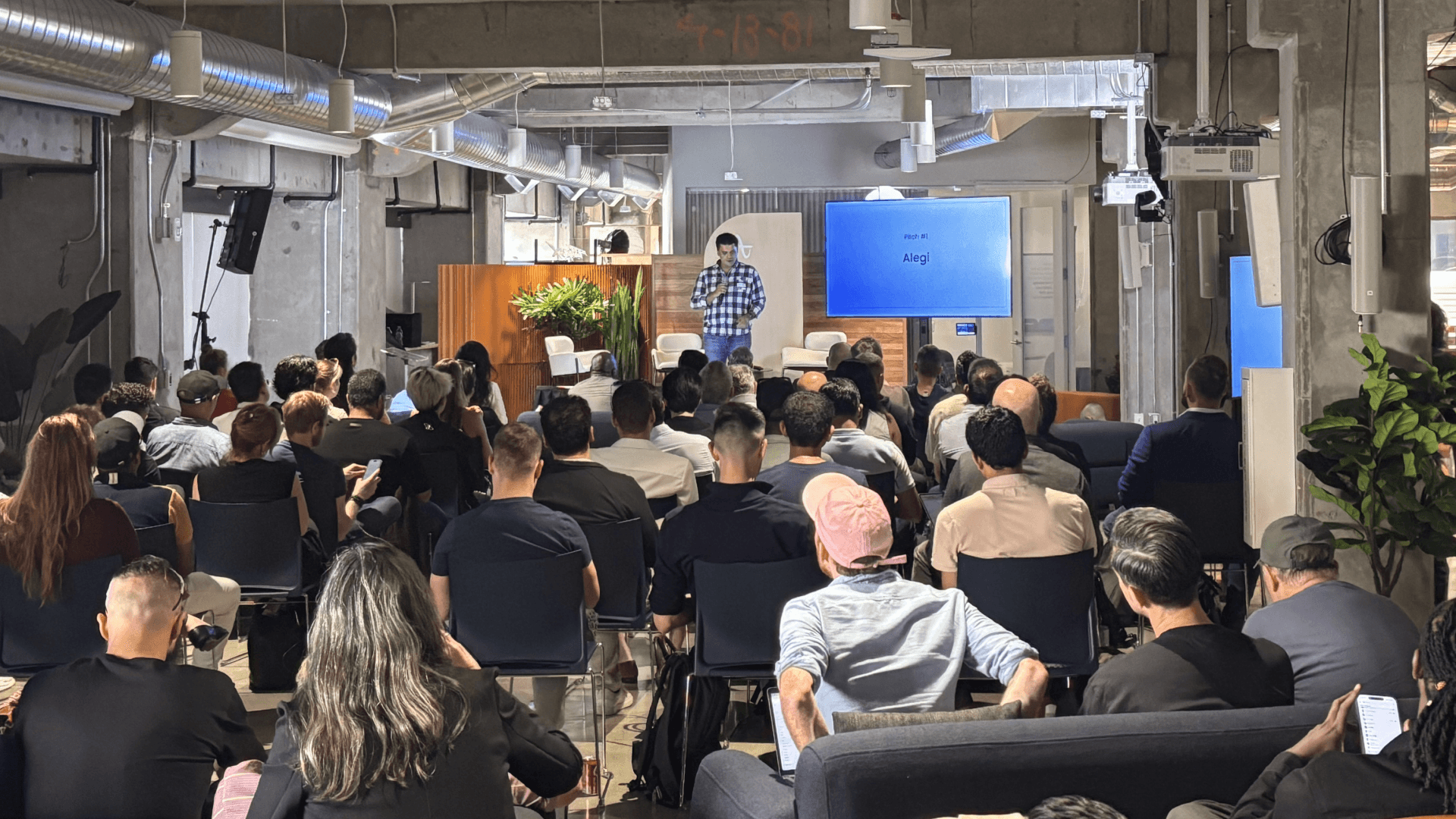 A crowd of founders, investors, and tech community members gather to watch a startup pitch
