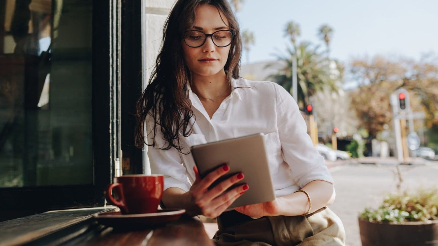 A lady using her tablet with a cup on the table