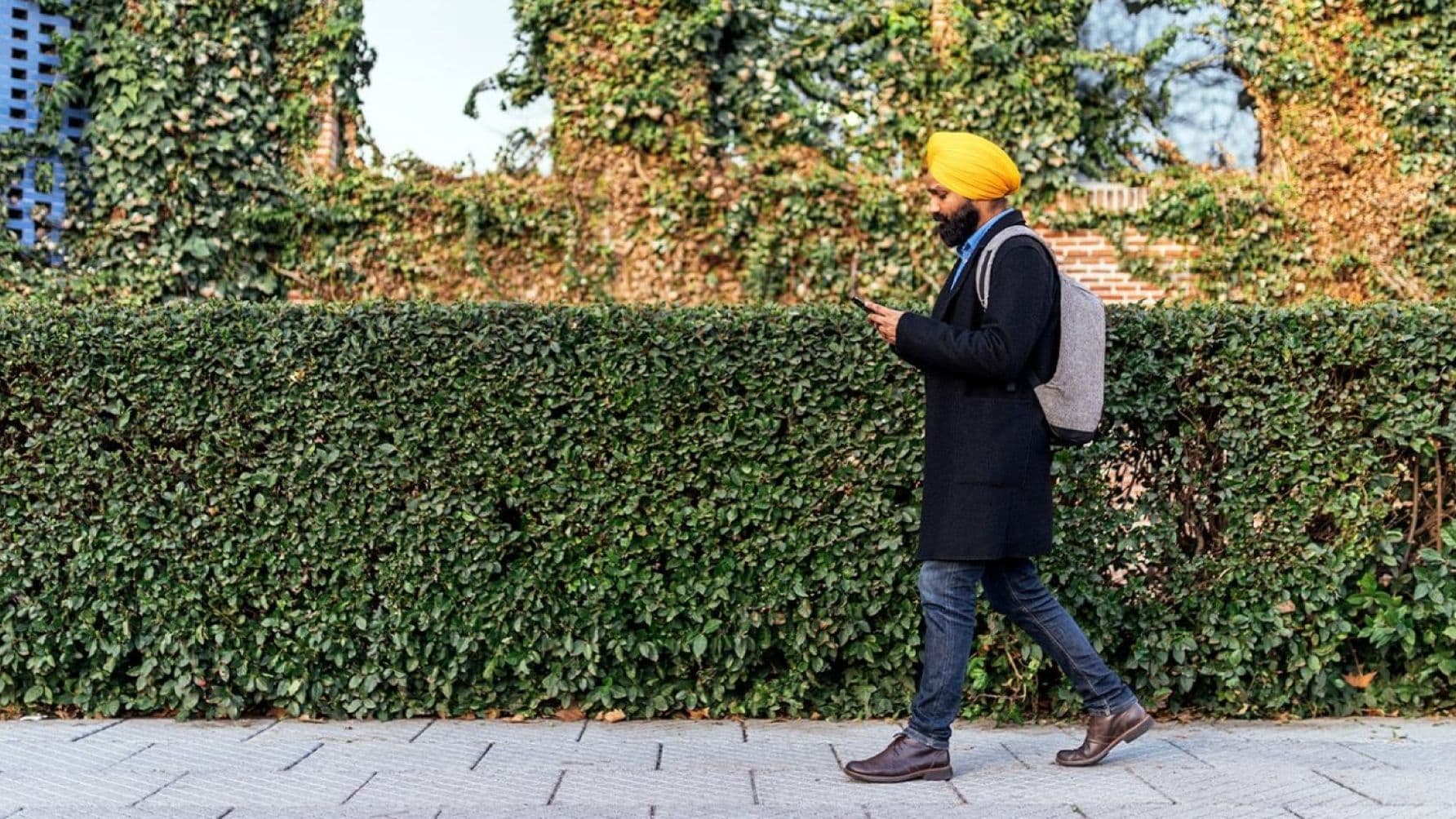 Man in a black coat walking with a bag on his back while using his smartphone