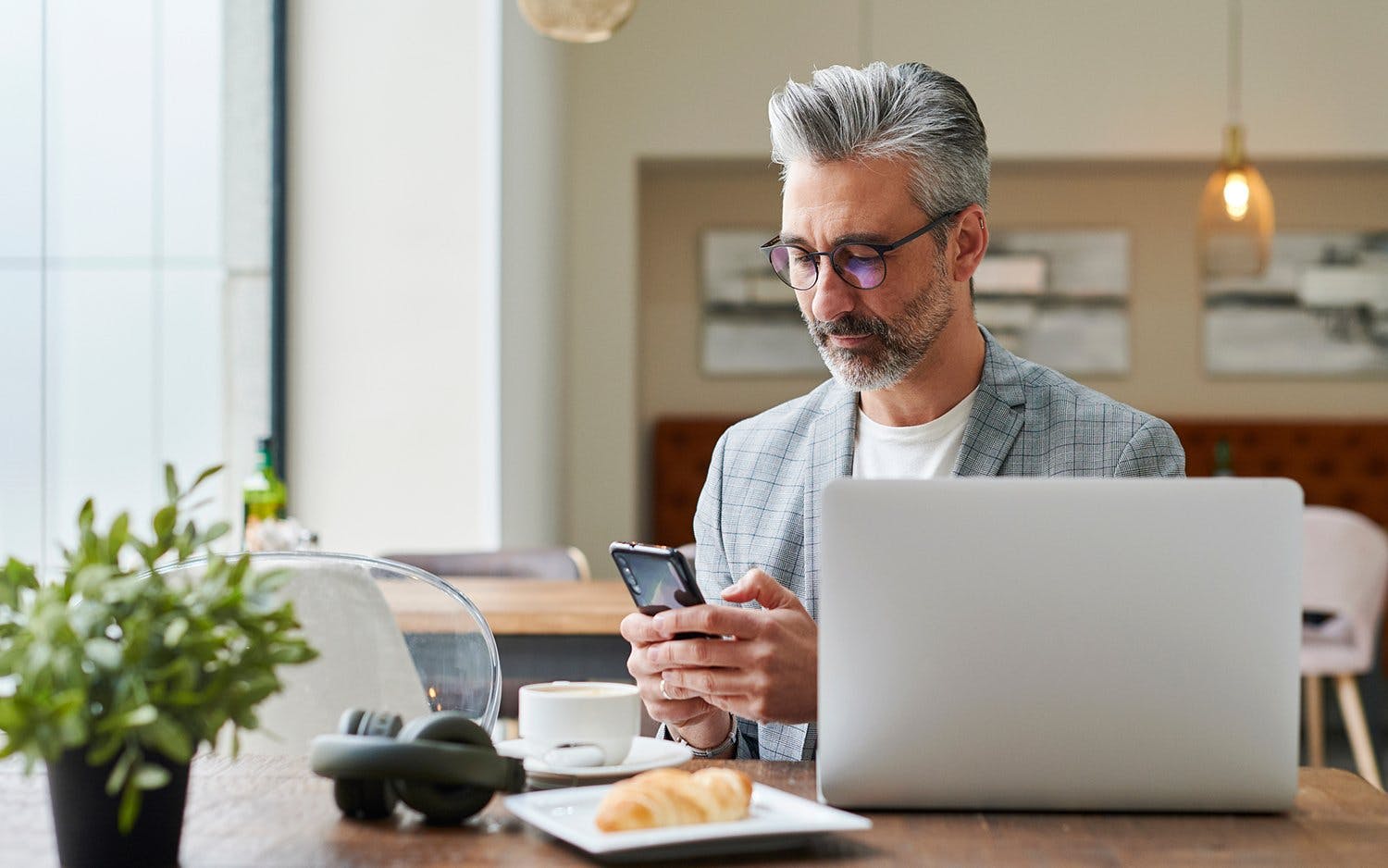 Man looking at mobile device while also sitting in front of laptop