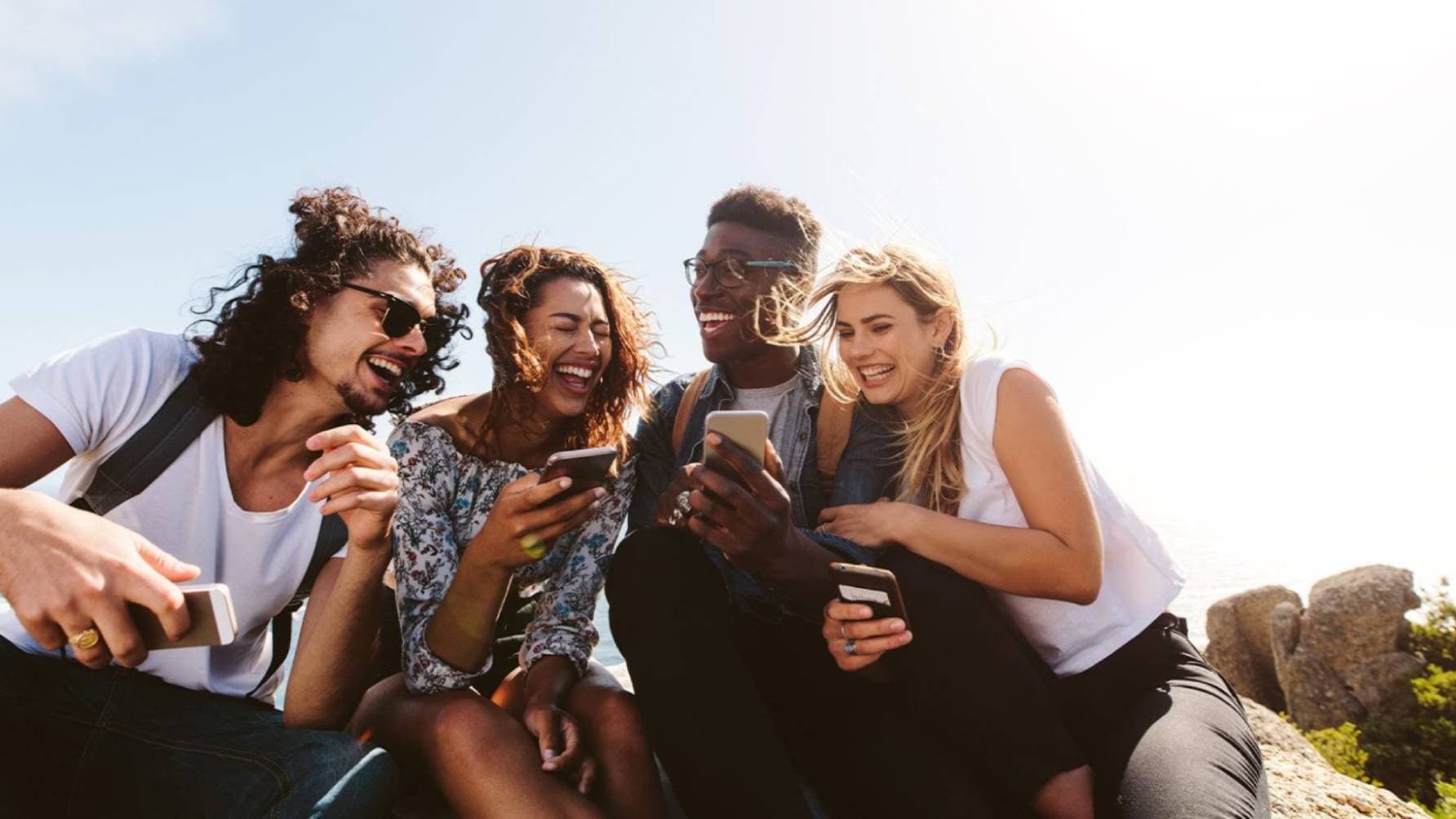 Four people seated on rock together with their phones smiling