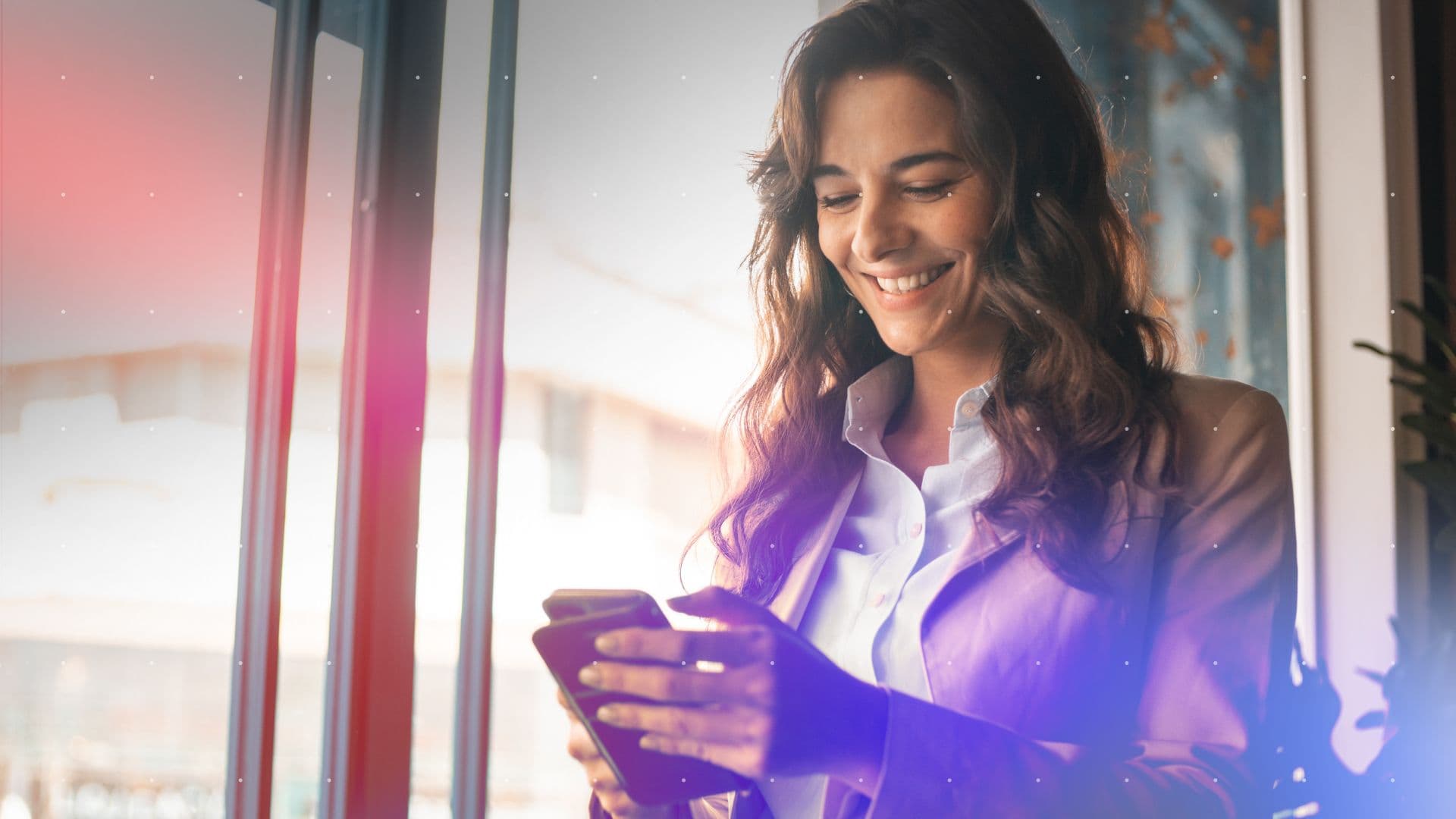 A professional-looking woman smiles while looking at her mobile device.