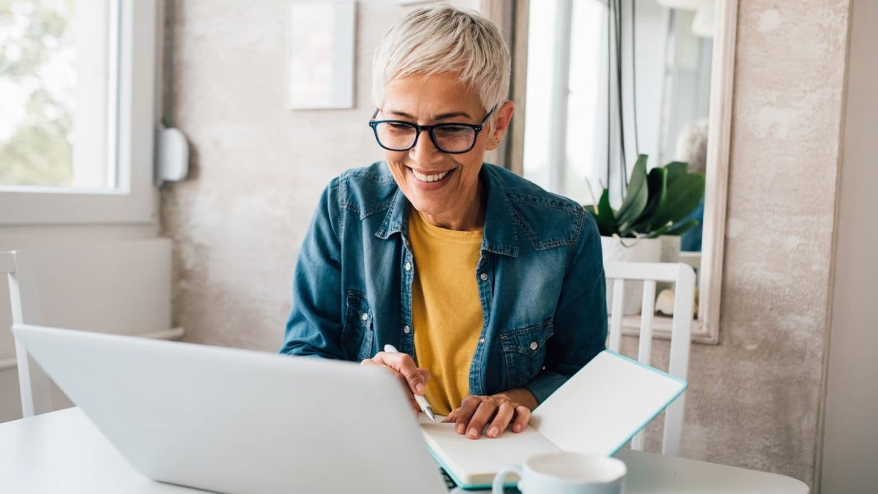 Woman holding a pen and a notebook while focusing on the laptop happily