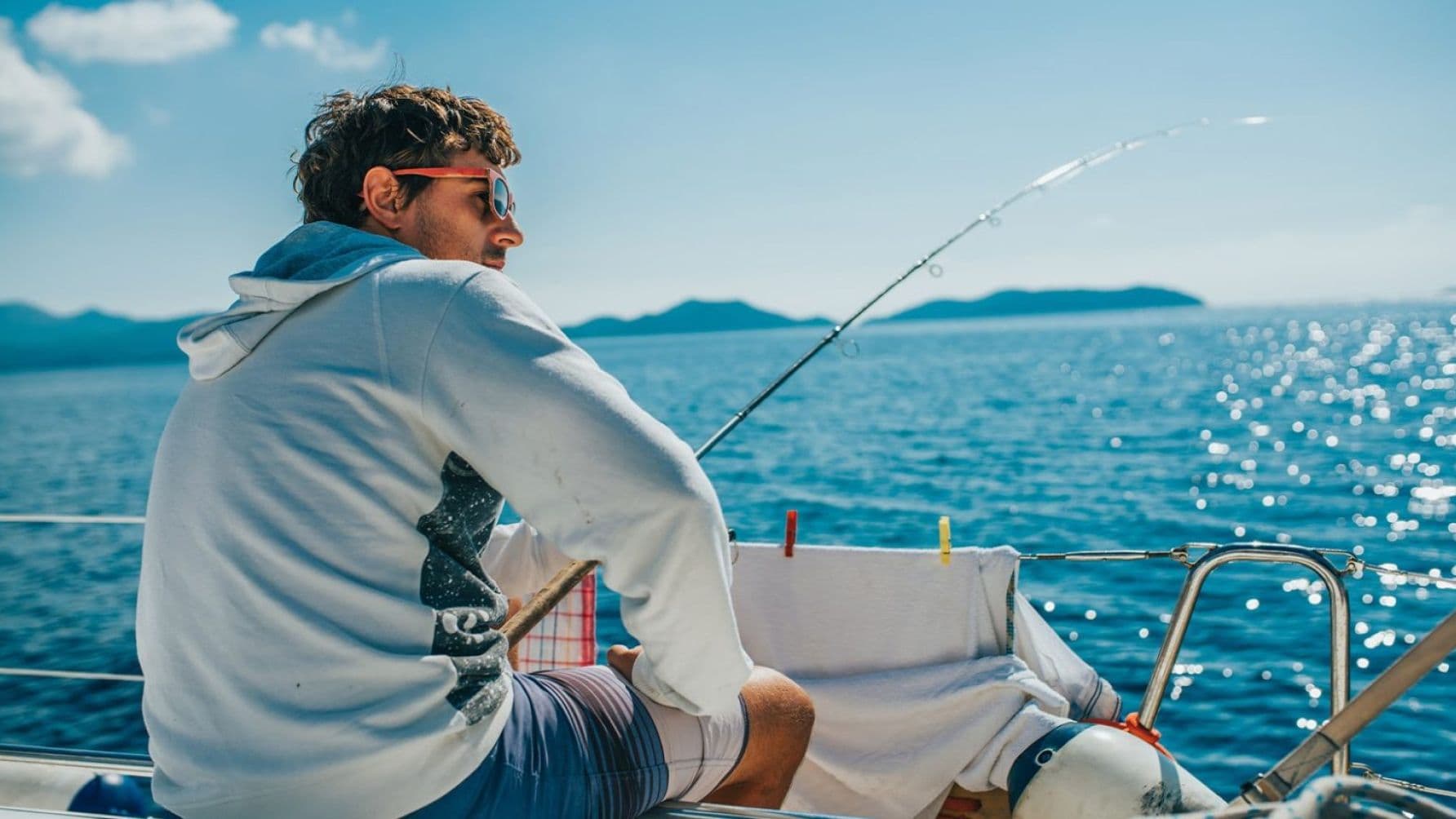 Man holding a fishing rod with some clothes hanging on the boat