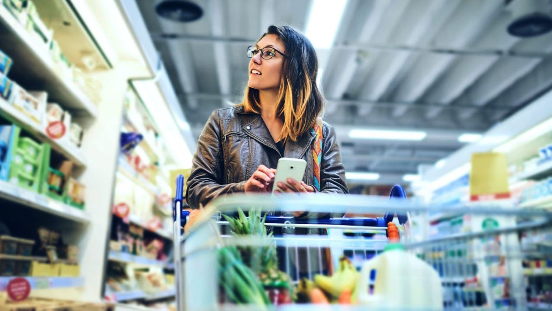 lady with a trolly doing shopping while using her smart phone